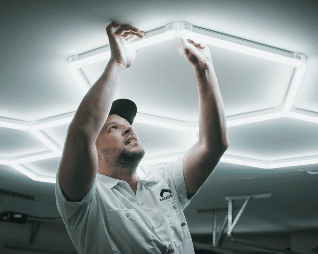 A professional Garage Up technician installing hexagon lights to a garage ceiling.