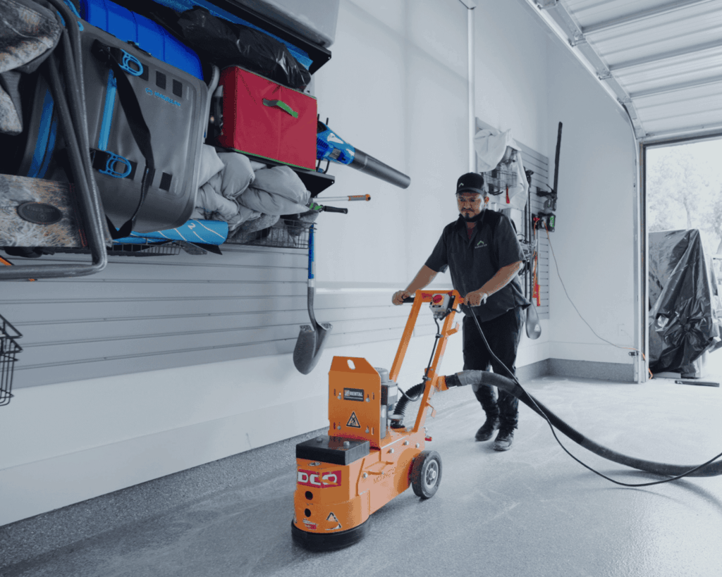 A photo fo a professional technician sanding down the epoxy on flooring done on a garage.