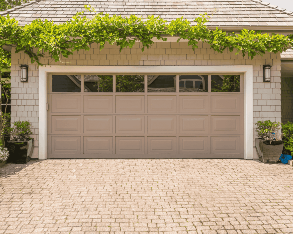 a tan two door garage door with partial view window panels and a tree vine growing above- expert garage renovations in jonestown